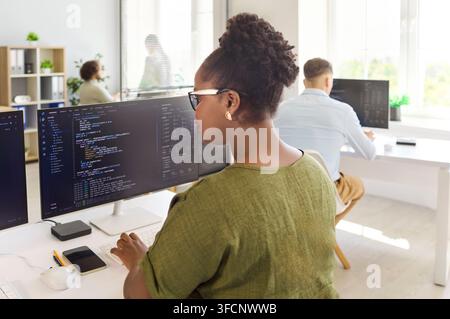 Programmers collaborating at modern office desks with code on dual monitors Stock Photo