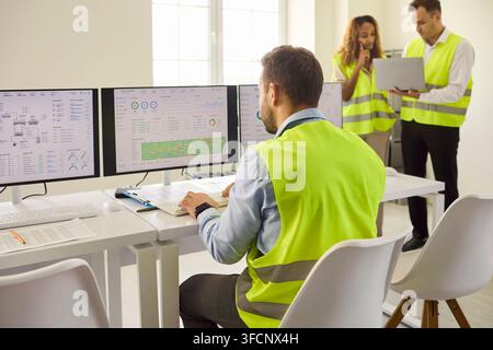 Engineers monitoring control room operations with analytics dashboards and safety Stock Photo