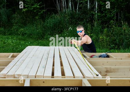 Wooden boards are measured by builder using tape measure during structural frame installation. Stock Photo