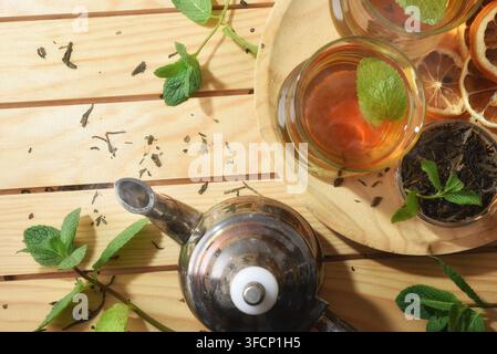 Detail of glass cups of hot green tea on a wooden plate with Moroccan-style metal teapot on wooden table with dried tea leaves and mint leaves outdoor Stock Photo