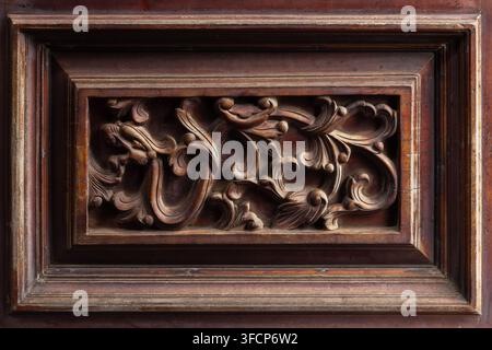 Ornate antique carved wood panel featuring intricate floral scrollwork in framed bas-relief, showcasing rich patina, detailed craftsmanship and vintag Stock Photo