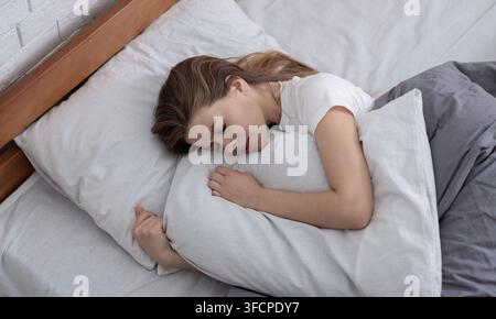 Top view of depressed young woman lying in bed and hugging her pillow Stock Photo