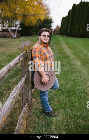 Young man in plaid shirt leans on a rustic fence Stock Photo