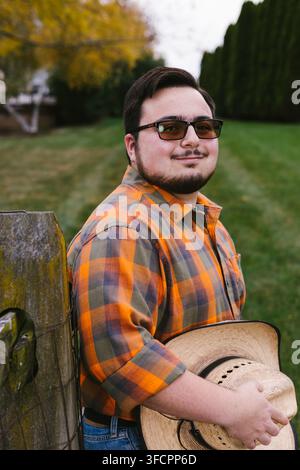 Young man in a plaid shirt smiling and holding a straw hat Stock Photo