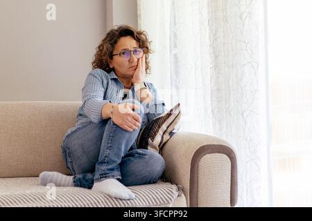 Worried mature woman sitting alone on a couch Stock Photo