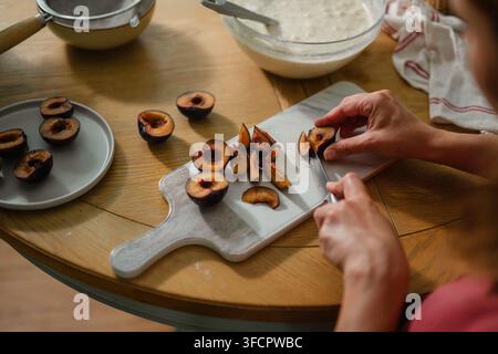 Woman slicing fresh plums on a wooden table, home baking Stock Photo