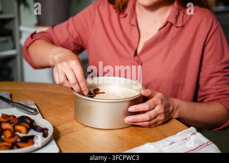 Woman places sliced plums on top of cake batter Stock Photo