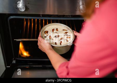 Woman carefully placing a fruit cake into a hot oven Stock Photo