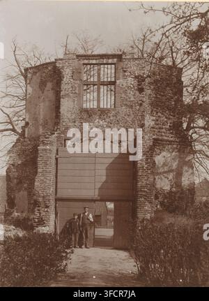 Gate of the castle ruin at Batenburg, photograph, annotation: 'Gem. Bemmel, Kasteel Doornburg', annotation: 'Batenburg, gem. Bemmel', Batenburg, 1906, photographer, Attributed to, paper, pasteboard, daylight collodion silver print, height 229 mm x width 170 mm, ruin of a dwelling, house, castle, gate, entrance, Kasteel Batenburg., A weathered stone and brick archway with a large wooden gate set into it stands amid leafless trees, the upper part of the structure showing a tall rectangular window with vertical bars and rough masonry around it, while the lower section reveals the closed wooden Stock Photo
