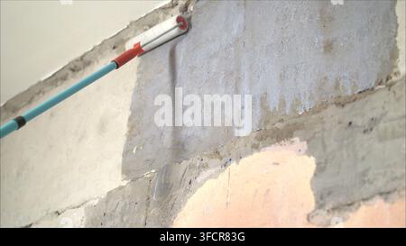 Long handle roller brush applying white primer paint on concrete wall with glass blocks in part of door frame, building and home renovation concept Stock Photo