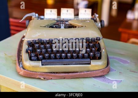 Vintage Manual Typewriter on Worn Table. Vintage manual typewriter with black keys and a worn olive body rests on a painted table in a softly blurred Stock Photo