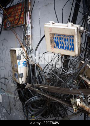 Chaotic mass of electrical cables, wires and junction boxes attached to a wall in Ho Chi Minh City, Vietnam, showing urban infrastructure. Stock Photo