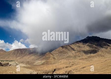 Dramatic storm clouds sweep over dry brown mountain ridges in a rugged highland landscape, with patches of blue sky and sunlight on the slopes. Stock Photo
