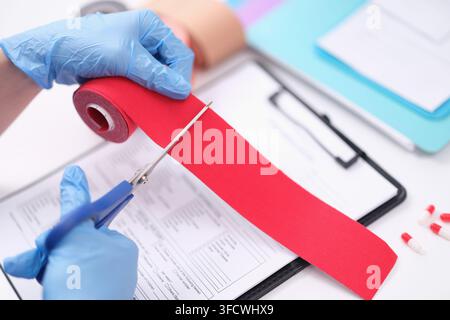 Physical therapist wearing gloves cutting red tape for kinesiotherapy closeup Stock Photo