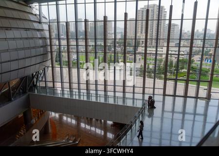 Modern building interior with glass walls overlooking cityscape. Two people walk calmly on reflective floors. Space feels open, airy, and professional Stock Photo
