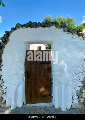 Rustic wooden gate framed by whitewashed stone wall under blue sky. Stock Photo