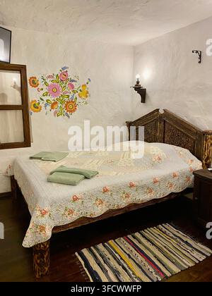 Rustic bedroom with carved wooden bed and colorful traditional floral decor. Stock Photo