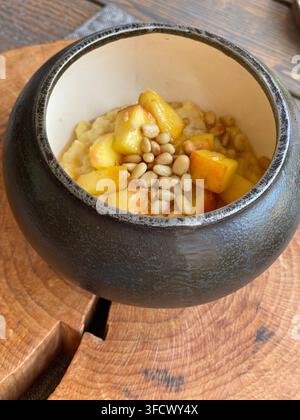Warm porridge topped with peaches and pine nuts served in rustic ceramic bowl. Stock Photo