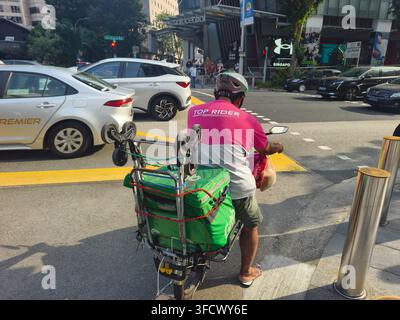 food delivery rider waiting at a traffic junction in Singapore,in Foodpanda "Top Rider" shirt while carrying a green GrabFood delivery bag on his vehicle Stock Photo