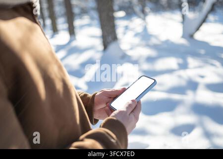 Close up of man using smartphone with white blank screen outdoors in sunny snowy park. Mobile communication, winter technology and online lifestyle co Stock Photo