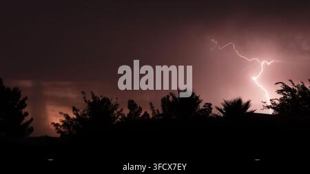 Lightning bolt coming from the sky at sunset with rain seen in the color of the sky near Sierra Vista Arizona during the monsoon season.. Stock Photo