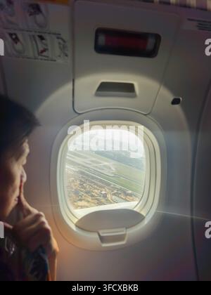 view from inside a commercial airplane cabin, a passenger looking thoughtfully out of an oval airplane window during takeoff, Singapore Stock Photo