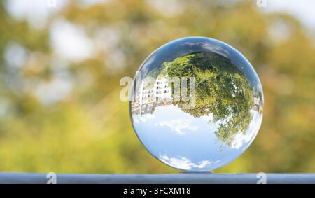Crystal sphere reflecting trees and residential buildings upside down creating artistic perspective and abstract urban nature composition Stock Photo