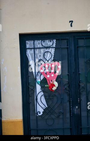 Decorative wrought iron doorway with a red heart ornament, white lace curtain and flowers on a traditional facade in Baeza, southern Spain Stock Photo
