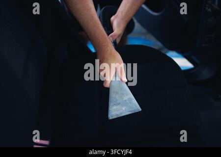 Person performing a thorough car interior detailing, using a wet vacuum cleaner to extract dirt and grime from the dark fabric seat, ensuring vehicle Stock Photo