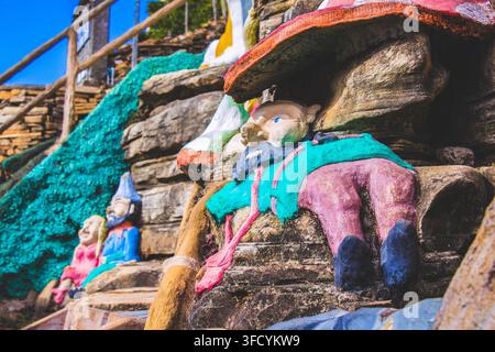 A whimsical collection of hand-painted garden gnome statues nestled among natural rock formations at an outdoor tourist attraction. Stock Photo