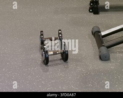 High-angle shot of two heavy black metal dumbbells placed neatly on a specked grey rubber gym floor. Essential equipment for free weight resistance tr Stock Photo
