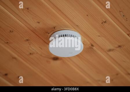 White smoke detector mounted on a wooden ceiling panel in a residential home. Stock Photo