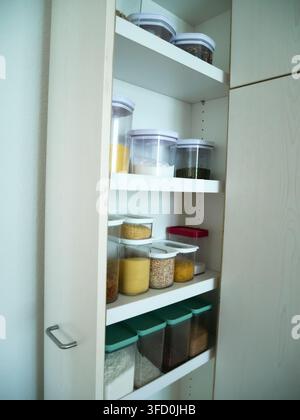 Kitchen cabinets and pantry shelves neatly organised with clear glass and plastic storage containers filled with dry goods and staples. Perfect for ho Stock Photo
