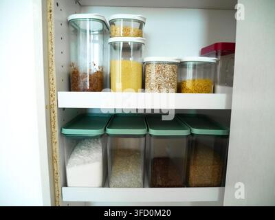 Kitchen cabinets and pantry shelves neatly organised with clear glass and plastic storage containers filled with dry goods and staples. Perfect for ho Stock Photo