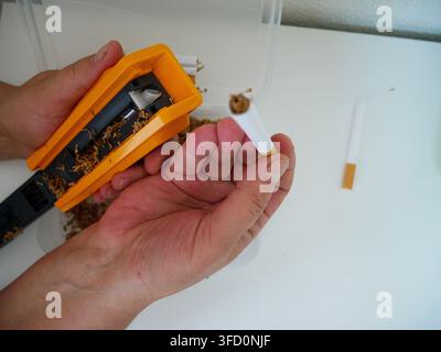 Complete DIY cigarette-making demonstration showing the rolling machine, tobacco supply, hands-on operation, and finished hand-rolled cigarettes Stock Photo