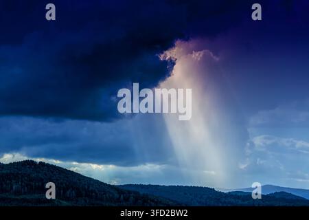 Dramatic sun rays breaking through storm clouds over mountain forest Stock Photo