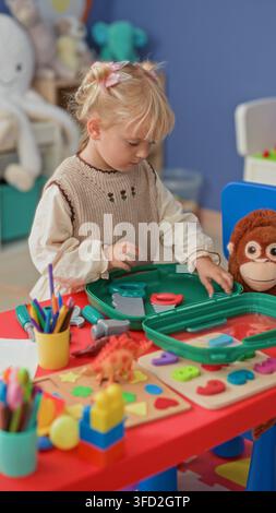Girl arranging toy puzzle pieces with hands on a red activity table in a playroom building; quiet concentration. Stock Photo