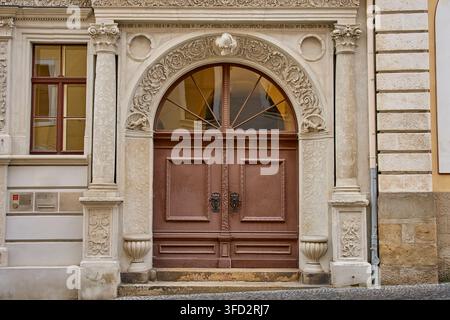Large wooden double door framed by detailed stone carvings, columns and arched window. Historic architecture and traditional building facade Stock Photo