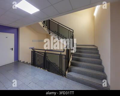 Indoor commercial building staircase featuring granite concrete steps and a modern black mesh metal balustrade. Clean architectural interior design of Stock Photo