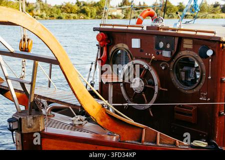 A detailed close-up shot of a classic wooden boat helm station featuring a traditional steering wheel, brass portholes, and navigation equipment on a Stock Photo