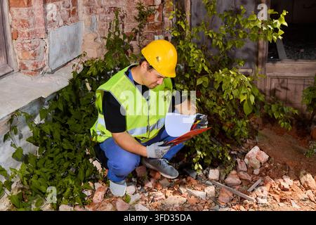 Construction inspector reviewing plans amid rubble at night Stock Photo