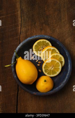 Fflat lay still life of Lemons. A whole lemon and a sliced lemon on a blue plate on a rustic wood table. Stock Photo