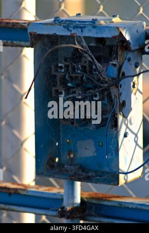 Exposed wiring and cobwebs fill a weathered blue utility box on a Long Beach gate. Stock Photo