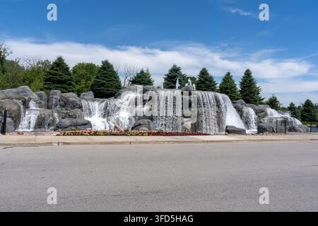 Close scenic view of a large decorative rock waterfall fountain surrounded by evergreen trees and colorful flower beds in Rosemont, Illinois. Stock Photo