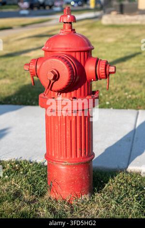 Close view of a bright red fire hydrant standing beside a sidewalk and grassy residential area on a sunny day. Stock Photo