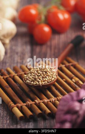Close-Up of Coriander Seeds in Wooden Spoon on Bamboo Mat with Garlic and Rustic Background Stock Photo