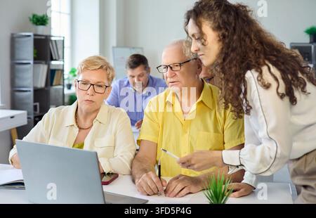 Teacher assisting senior students during laptop training in light office classroom Stock Photo