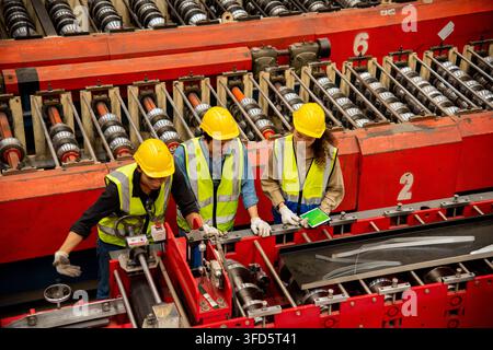 Engineer and operator wearing a safety suit maintaining machine in industrial metal sheet factory, team worker walk teaching help friend operate contr Stock Photo