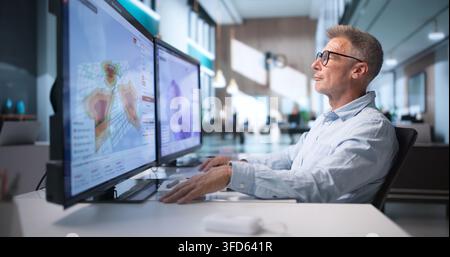 Environmental Scientist Analyzes Flood Risk Maps On Computer For Disaster Planning. Stock Photo