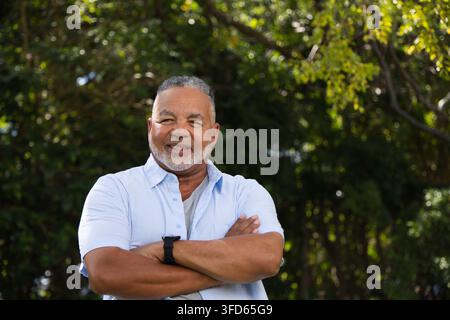 Mature African man standing smiling arms crossed in park wearing light blue shirt and wristwatch Stock Photo